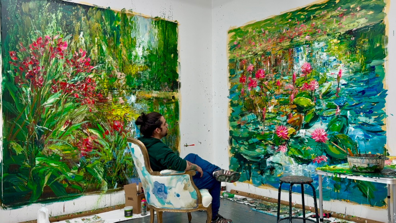 A male artist sitting in a chair in front of two of his flower paintings