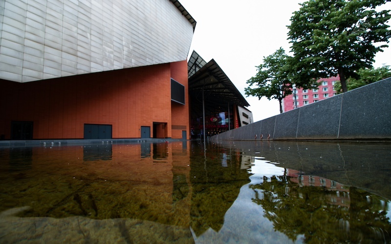 Flooded plaza outside a modern building, with water pooling near the entrance.