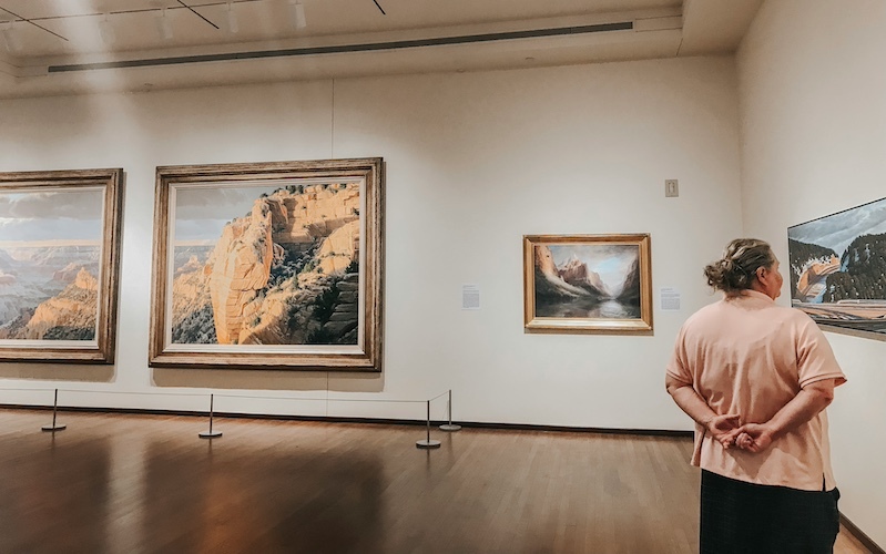 woman looking at landscape artworks installed in a white gallery space