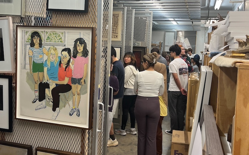 A group of people in artwork storage with paintings hanging on dividers